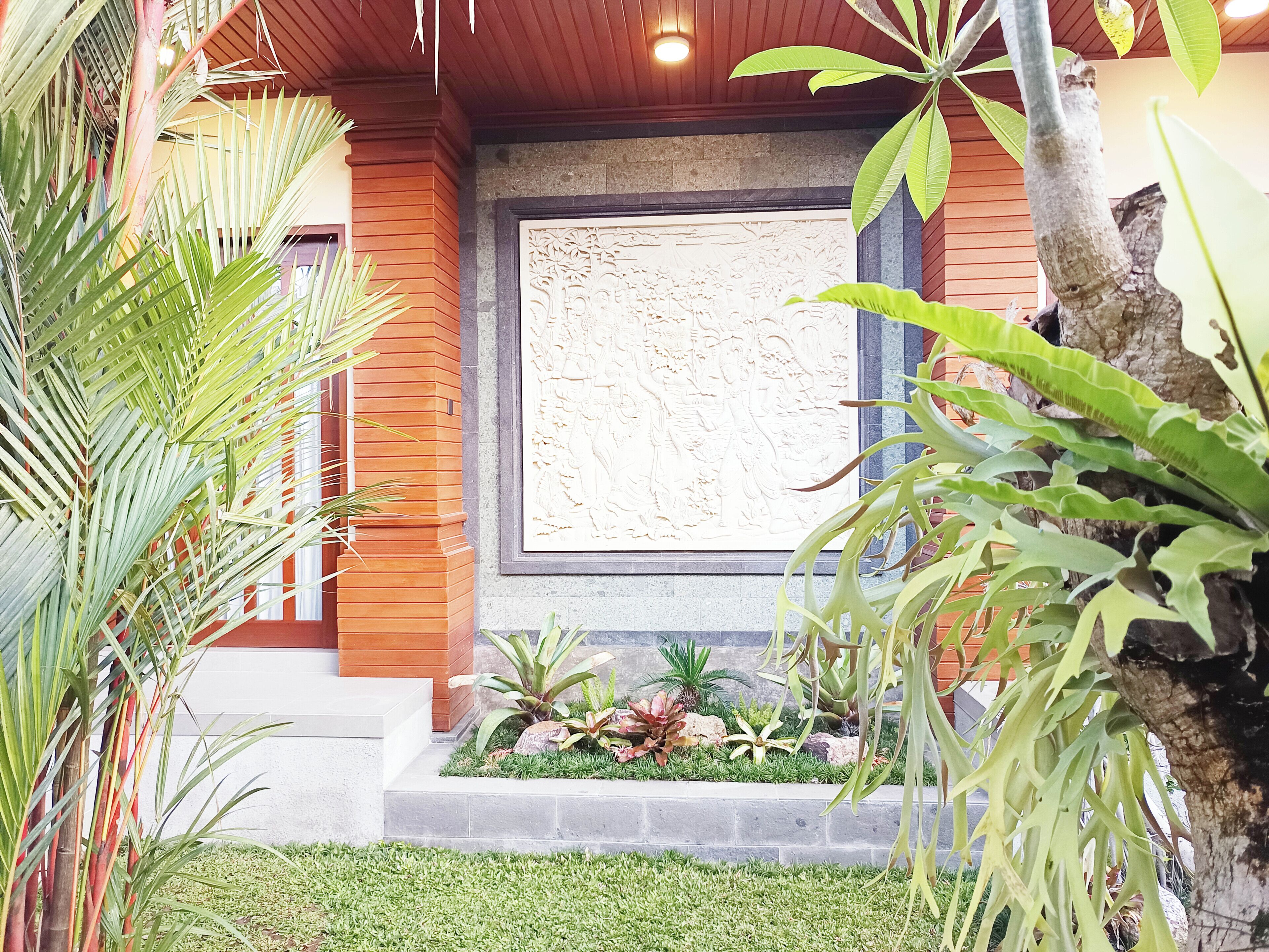 A modern building with a wooden facade, a stone wall with a carved relief, and a landscaped garden with various plants.