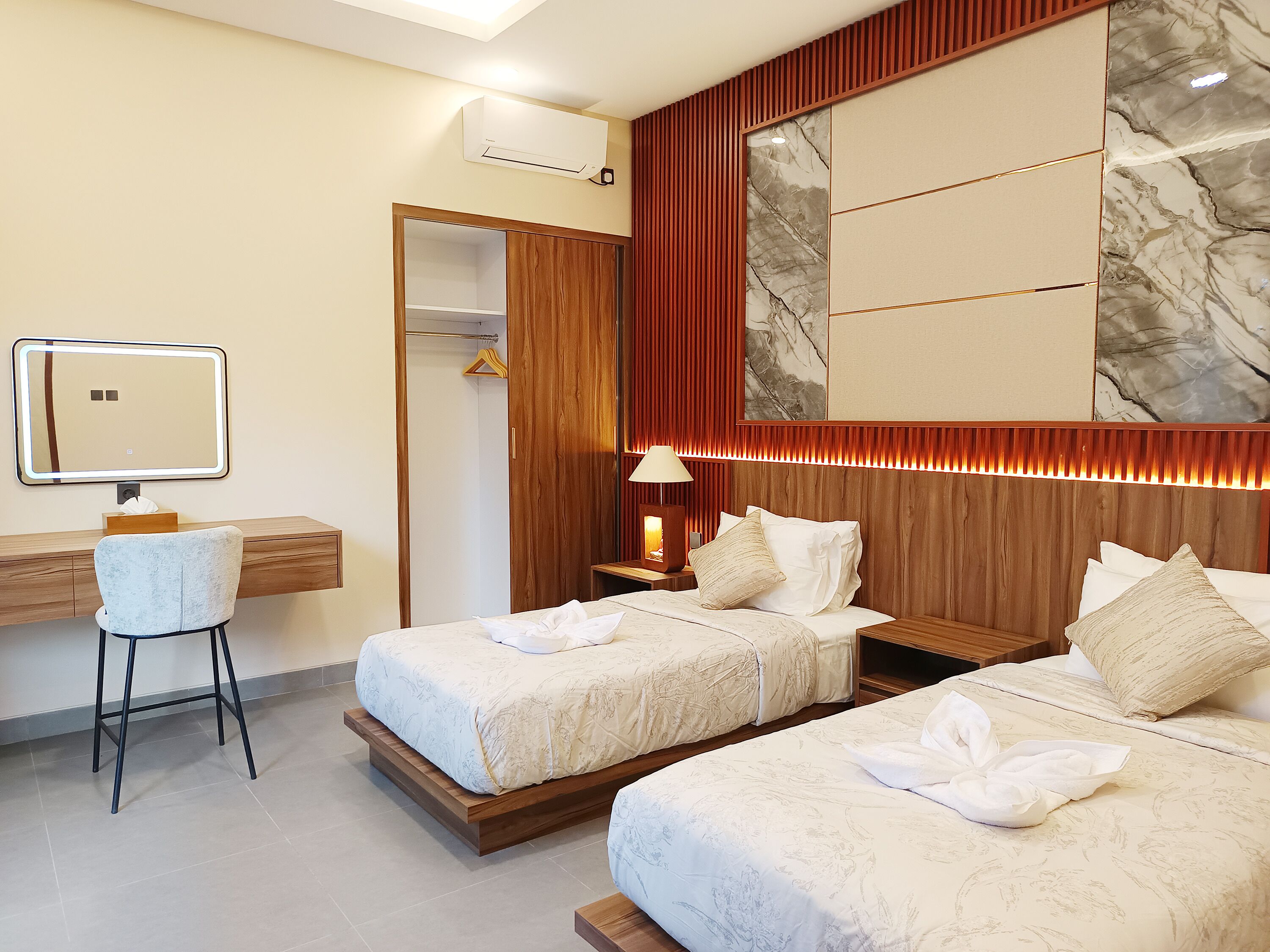 Ein Hotelzimmer mit zwei Betten, einem Schreibtisch mit Spiegel, einem Stuhl, einem Kleiderschrank und einer Wandklimaanlage.