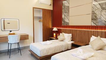 A hotel room with two beds, a desk with a mirror, a chair, a wardrobe, and a wall-mounted air conditioner.