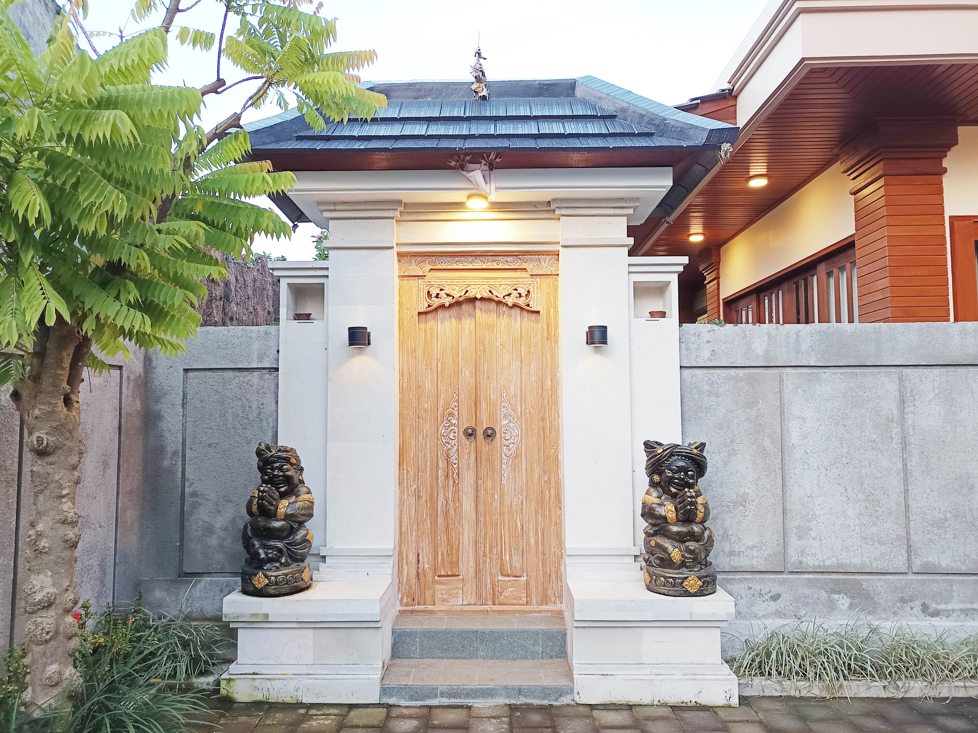 Uma porta de madeira tradicional com um detalhe decorativo no topo, ladeada por duas estátuas de cada lado.
