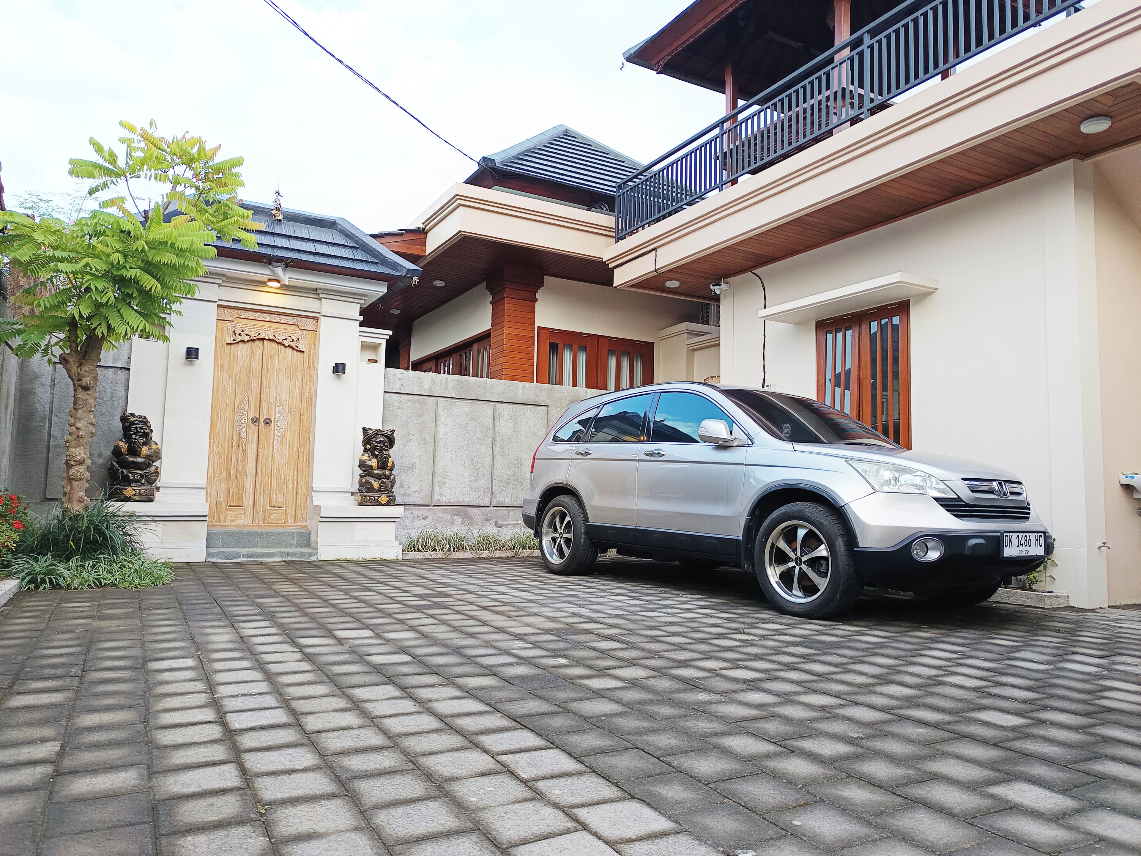 A residential area with a paved driveway, a parked car, and a traditional wooden gate.