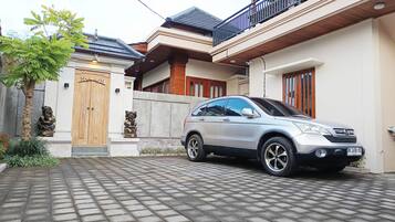 A residential area with a paved driveway, a parked car, and a traditional wooden gate.