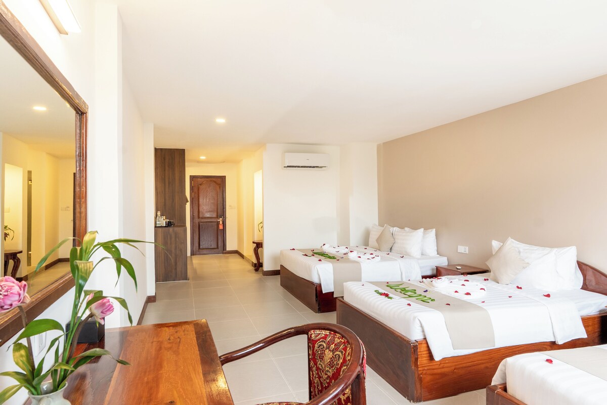 A hotel room with two beds, a wooden desk, a chair, a mirror, and a potted plant.