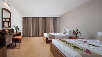 Quarto de hotel com duas camas, uma escrivaninha, uma cadeira, um espelho e uma janela grande com cortinas.