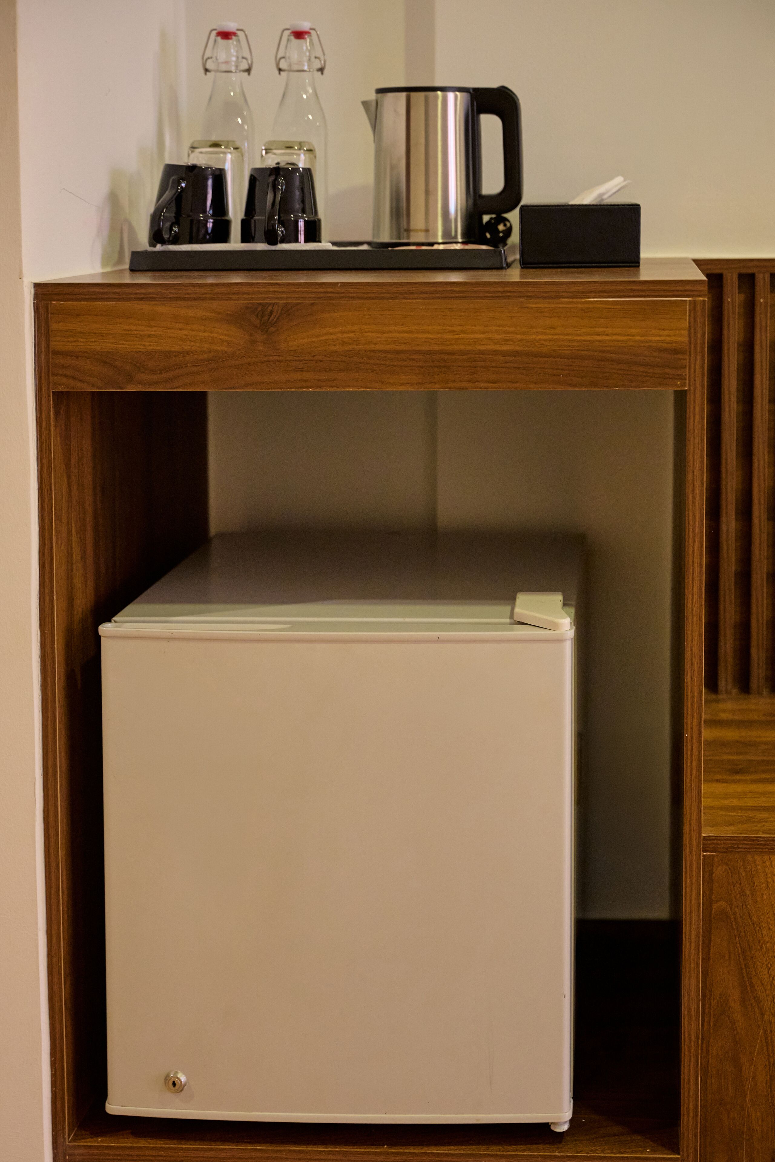 Una mesa de madera con un refrigerador blanco y tres botellas encima.