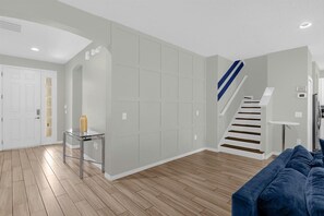 Een moderne woonkamer met een trap, een glazen salontafel en een blauwe bank.