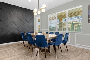 A dining area with a wooden table, blue upholstered chairs, and a black geometric wall. - 14-bedroom house in Davenport close to Disney animal kingdom. (Davenport)