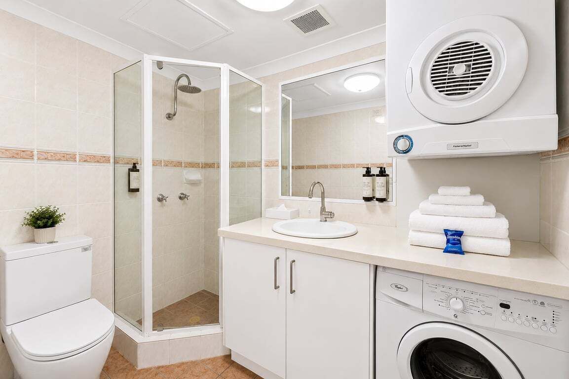 Une salle de bain moderne avec une douche à parois de verre, un lavabo avec un miroir, des toilettes et un lave-linge.