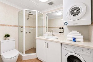 A modern bathroom with a glass-enclosed shower, a sink with a mirror, a toilet, and a washing machine. - Modern CBD Retreat | Walk to Shops & Dining (Brisbane)