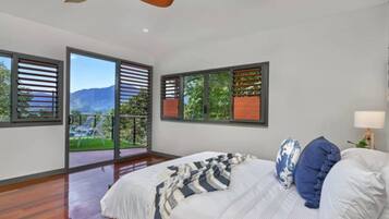 A bedroom with a bed, a ceiling fan, and a view of a balcony.