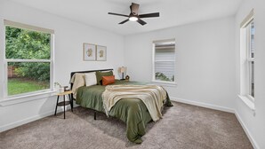 Un dormitorio con cama, ventilador de techo, ventana y una mesita.