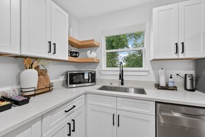 A modern kitchen with white cabinets, a stainless steel sink, a microwave, and a window with a view of trees. - Executive 3BR Home, King Suite, Near Hospitals & Historic Downtown Mansfield (Mansfield)