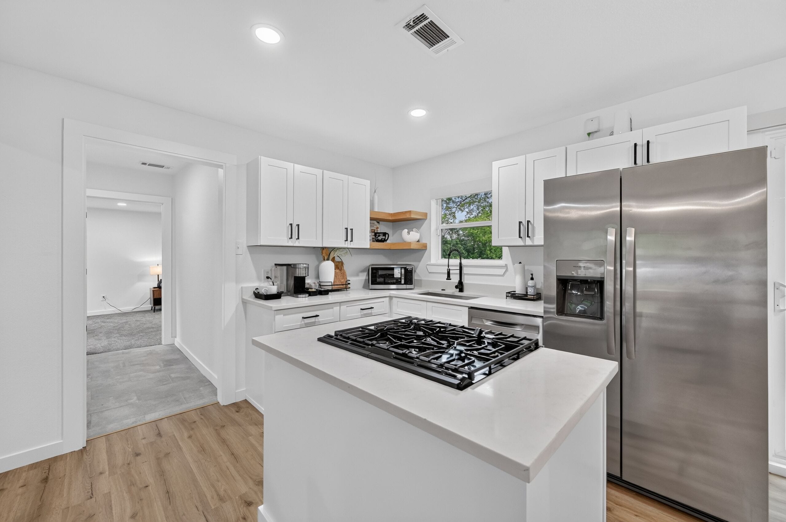A modern kitchen with white cabinetry, a stainless steel refrigerator, and a central island with a gas stove.