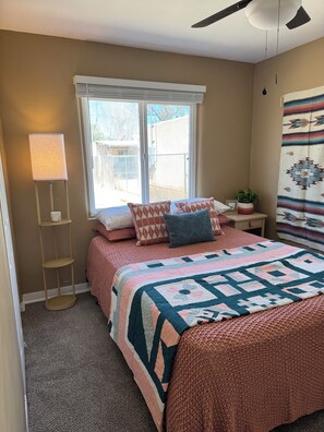A bedroom with a bed, a standing lamp, a window, and a wall-mounted ceiling fan. - Charming Retreat in ABQ's North Valley-close to Old Town and Balloon Fiesta Park (Albuquerque)