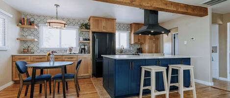 Una cocina moderna con vigas de madera, una isla central, taburetes de bar y un comedor con sillas.