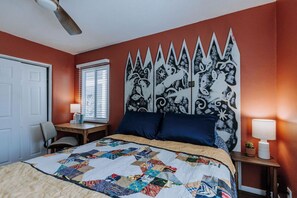 A bedroom with a quilted bedspread, a decorative headboard, a desk with a chair, and a window with blinds. - Charming Retreat in ABQ's North Valley-close to Old Town and Balloon Fiesta Park (Albuquerque)