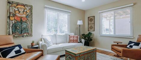 A living room with a sofa, two armchairs, a patterned ottoman, and a large painting on the wall.