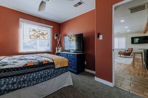 Een slaapkamer met een bed, een dressoir, een televisie en een raam met jaloezieën.