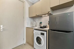 Eine kleine Küche mit Waschmaschine, Edelstahlkühlschrank und beigen Schränken.