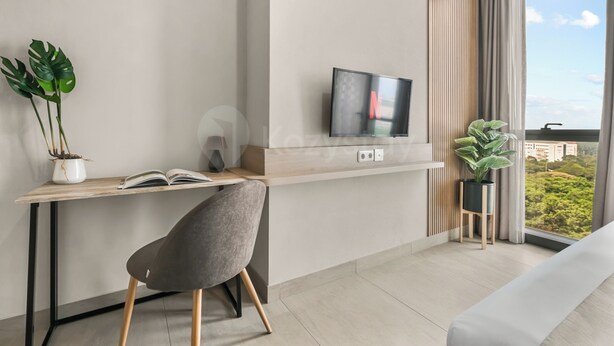 A modern room with a desk, chair, TV, and large windows with a view. - Narela by Kozystay - Kemayoran (Central Jakarta)