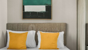 A bed with white and mustard-colored pillows, a grey headboard, and a wall-mounted abstract painting. - Narela by Kozystay - Kemayoran (Central Jakarta)