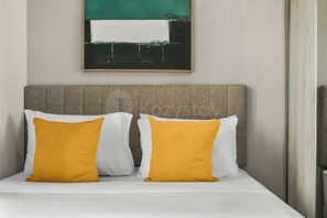A bed with white and mustard-colored pillows, a grey headboard, and a wall-mounted abstract painting. - Narela by Kozystay - Kemayoran (Central Jakarta)