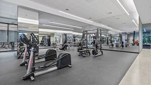 A gym with cardio equipment, weight machines, and mirrors on the walls. - Narela by Kozystay - Kemayoran (Central Jakarta)