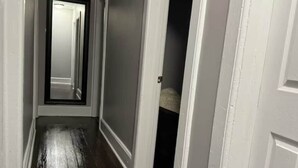 Un couloir doté d’un plancher en bois, de murs blancs et d’une porte donnant sur une pièce sombre.