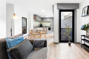 Ein modernes Wohnzimmer mit einer Couch, einem Esstisch mit Stühlen, einer Küche im Hintergrund und einer Zimmerpflanze.