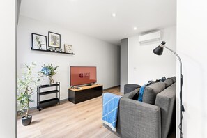 Ein modernes Wohnzimmer mit Flachbildfernseher, Sofa, Stehlampe und einer kleinen Pflanze.