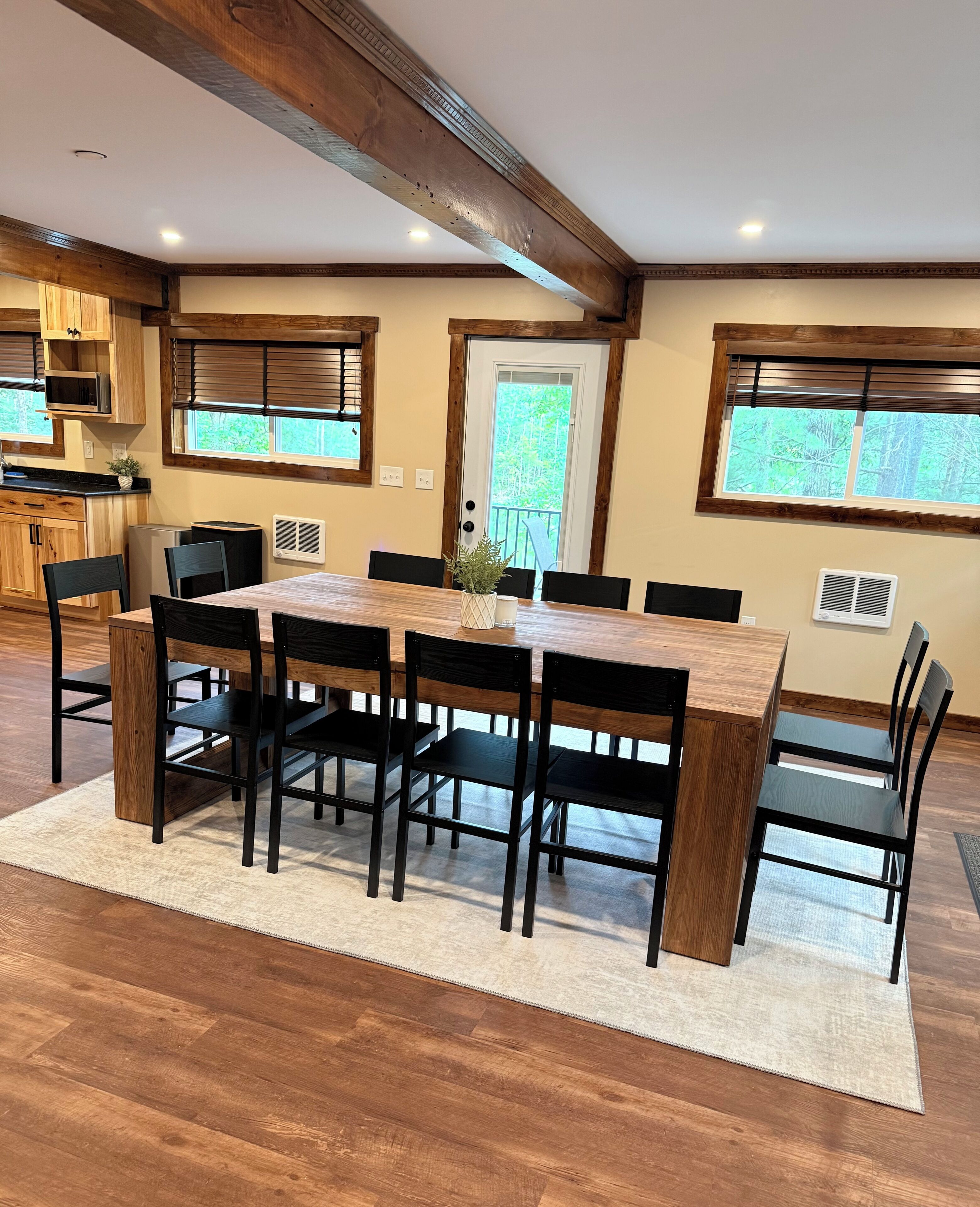 Un comedor con mesa y sillas de madera, una cocina al fondo y una puerta que da a un balcón.