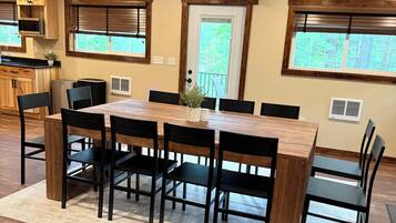 Un comedor con mesa y sillas de madera, una cocina al fondo y una puerta que da a un balcón.
