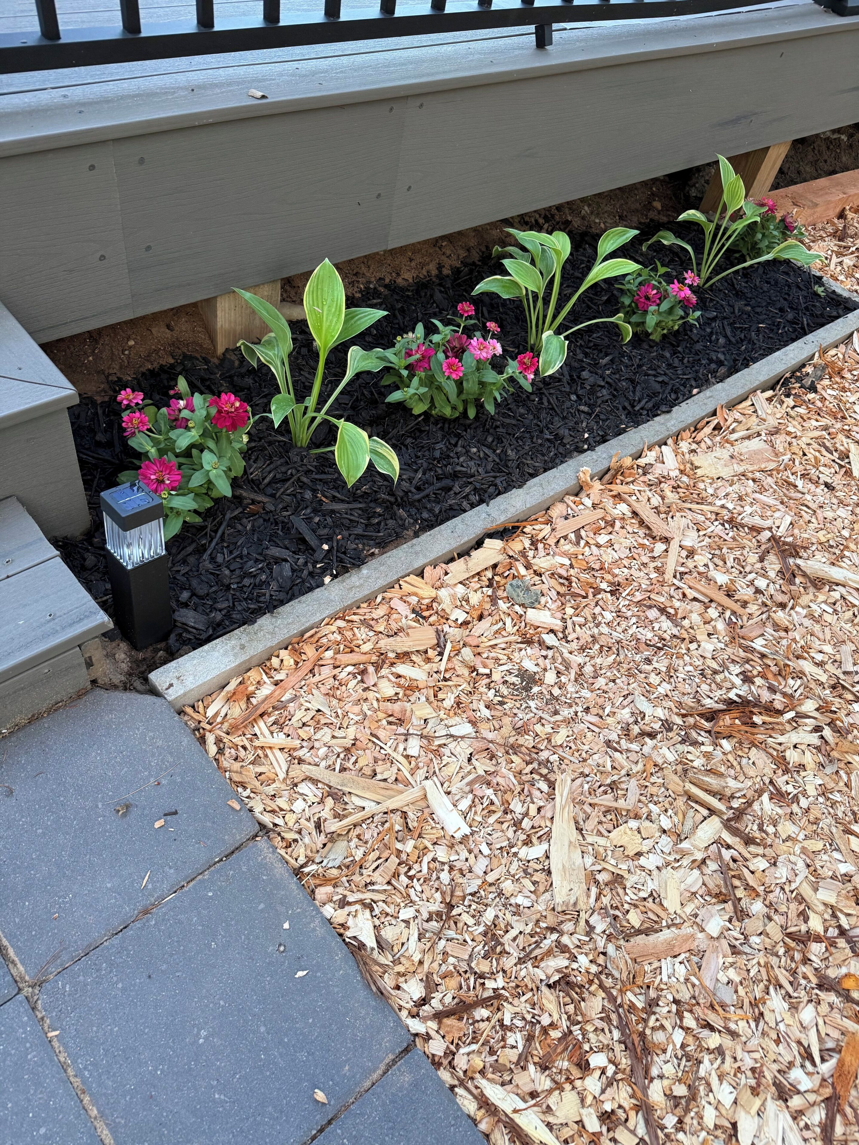 Ein Blumenbeet mit Pflanzen und Mulch, eine Bank und ein Weg.