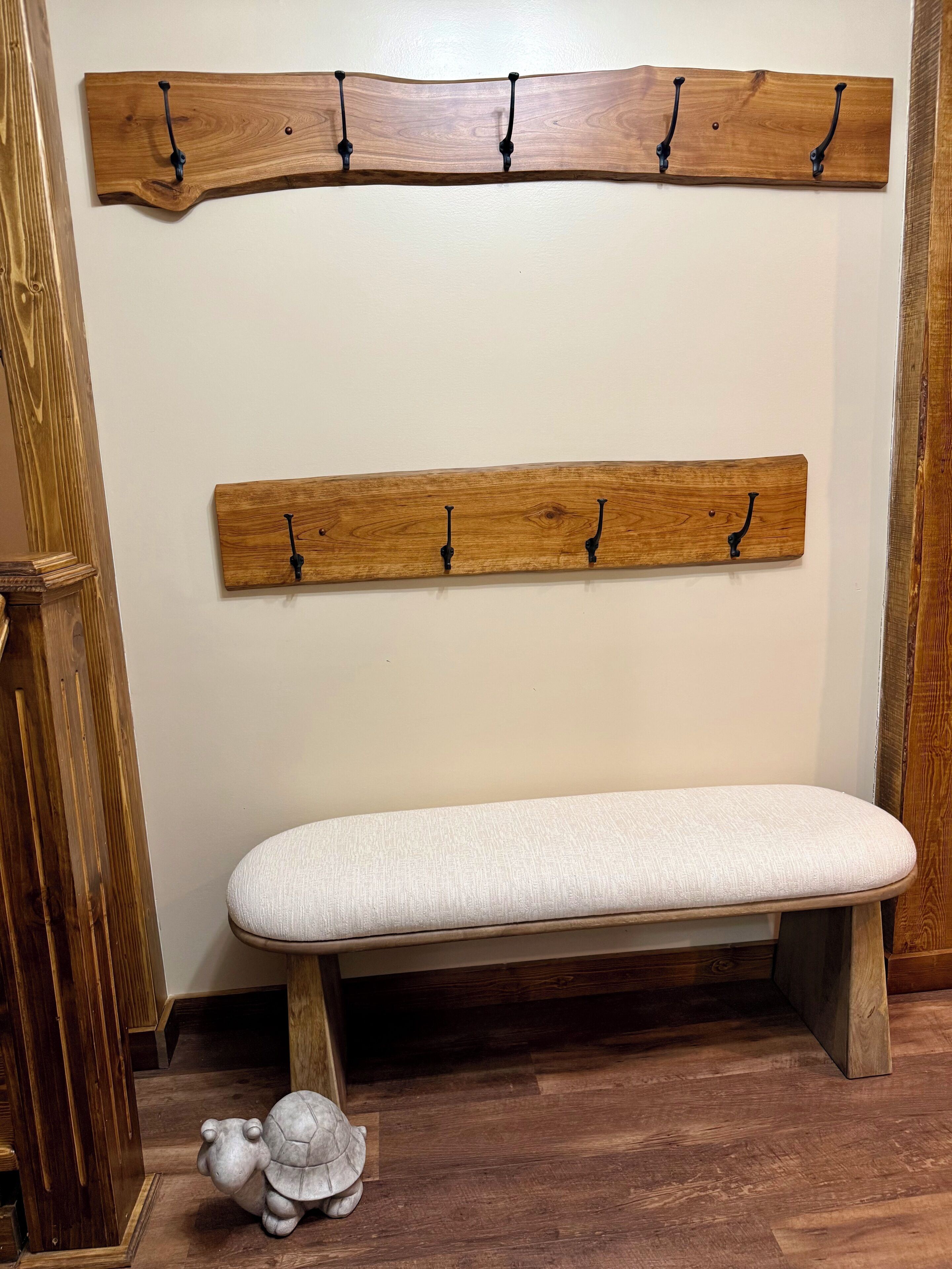 A wooden bench with a white cushion, a wooden wall-mounted rack with hooks, and a small turtle figurine on the floor.