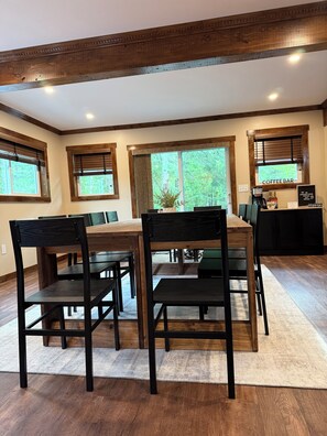 A dining area with a wooden table and chairs, a coffee bar with a sign, and large windows with blinds. - Maple Pond Retreat - Sleeps 14 - Kayaks, Fire Pit & Wildlife (Gaylord)