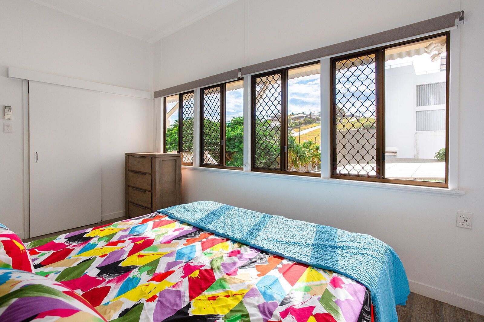A bedroom with a bed, a dresser, and a window with a view of greenery.