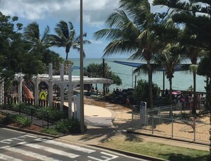 A beachside area with a pedestrian walkway, palm trees, and a view of the ocean. - Wake to Sunrises on Yeppoon’s Beachfront (Yeppoon)