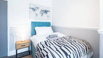 A neatly made bed with a striped blanket, a bedside table with a lamp, and a world map artwork on the wall.