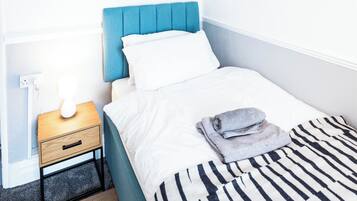 A neatly made bed with a striped blanket, a world map artwork on the wall, a bedside table with a lamp, and a small drawer.