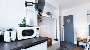A compact kitchenette with a microwave, toaster, and a hanging plant.