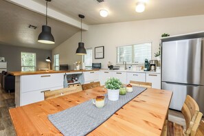A modern kitchen with a wooden island, stainless steel appliances, pendant lighting, and a dining area with a patterned runner.