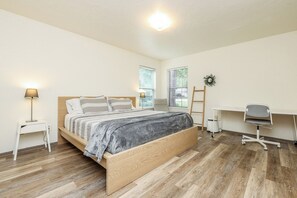 A bedroom with a bed, bedside table, desk, chair, and a window with blinds.