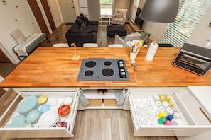 A kitchen with a built-in stove, wooden table, and two open storage drawers with dishes and utensils.