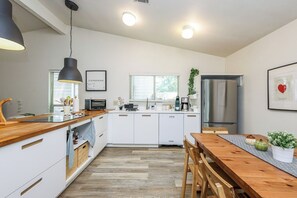 A modern kitchen with white cabinetry, a wooden countertop, a built-in oven, a stainless steel refrigerator, and a dining table with chairs.