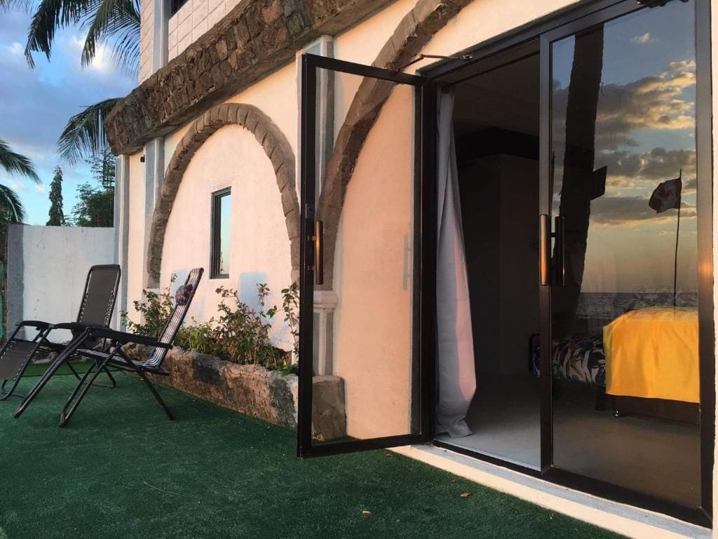 A room with a bed, a window, and a sliding glass door leading to an outdoor area with a chair and a small table.