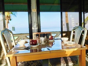A table set for two with a view of the sea, a green roof, and a patterned tablecloth.