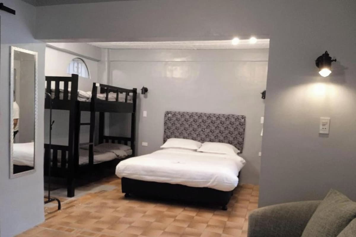 A room with a bunk bed, a single bed, a sofa, and a small table.