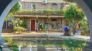 A stone building with a wooden door, a small garden, and a water feature in front.