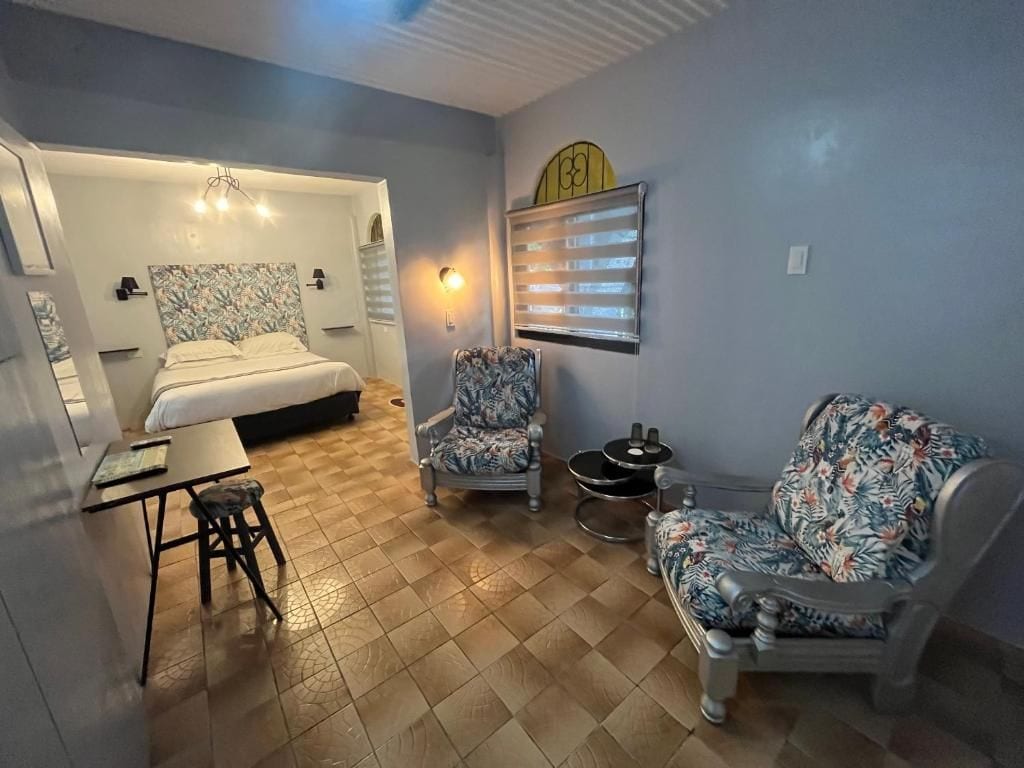 A room with a bed, two chairs, a small table, and a wall-mounted heater.