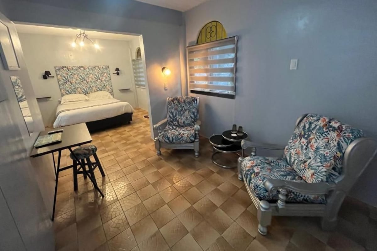 A room with a bed, two chairs, a small table, and a wall-mounted heater.